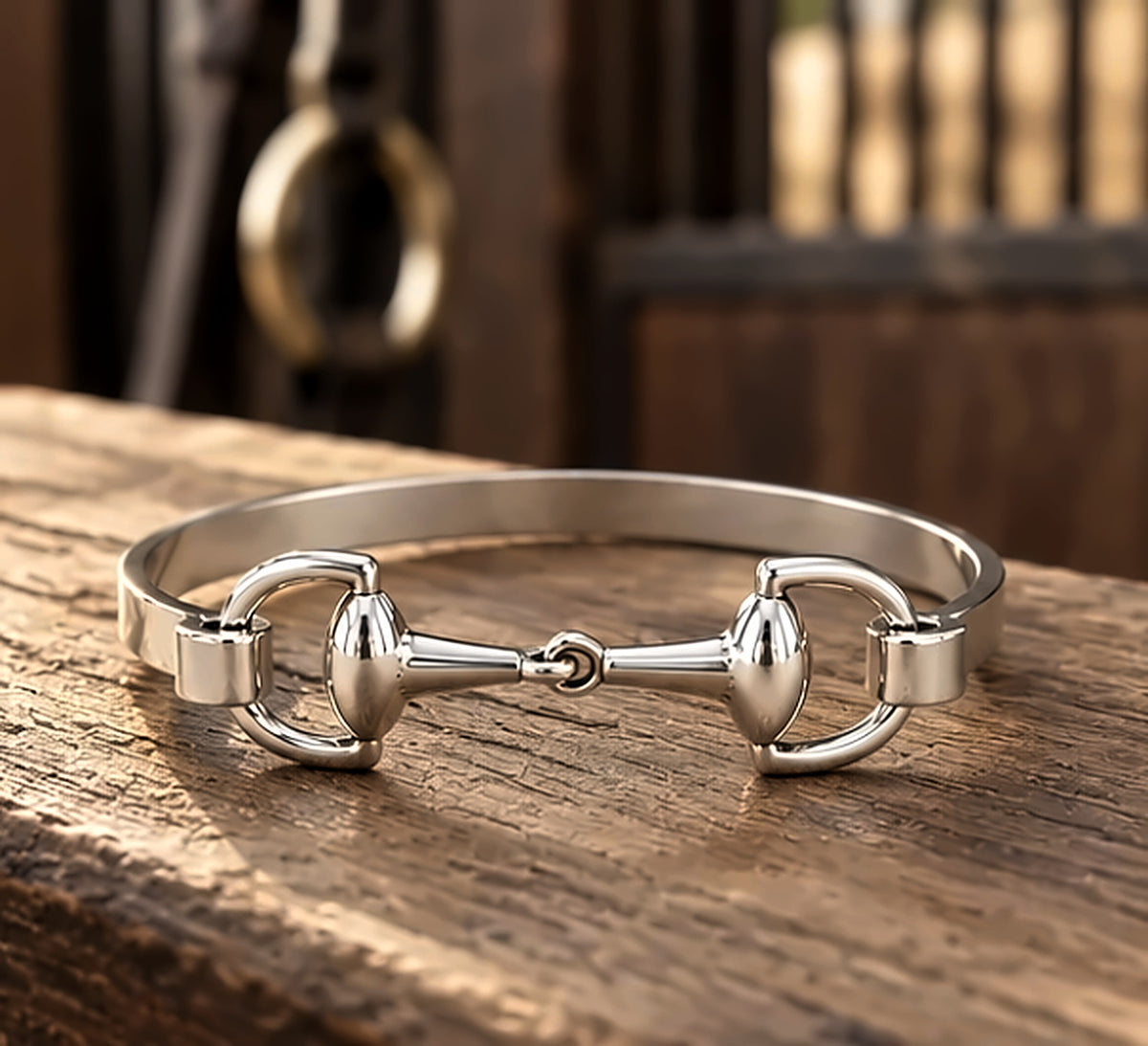 Silver snaffle bit bracelet lying flat on a wooden tack trunk in the barn