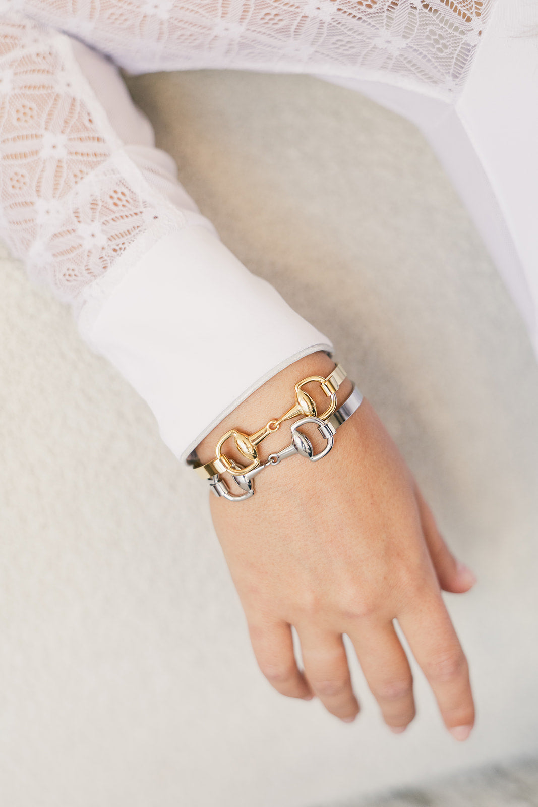 Silver and gold snaffle bit bracelets stacked on a wrist with a white lace sleeve